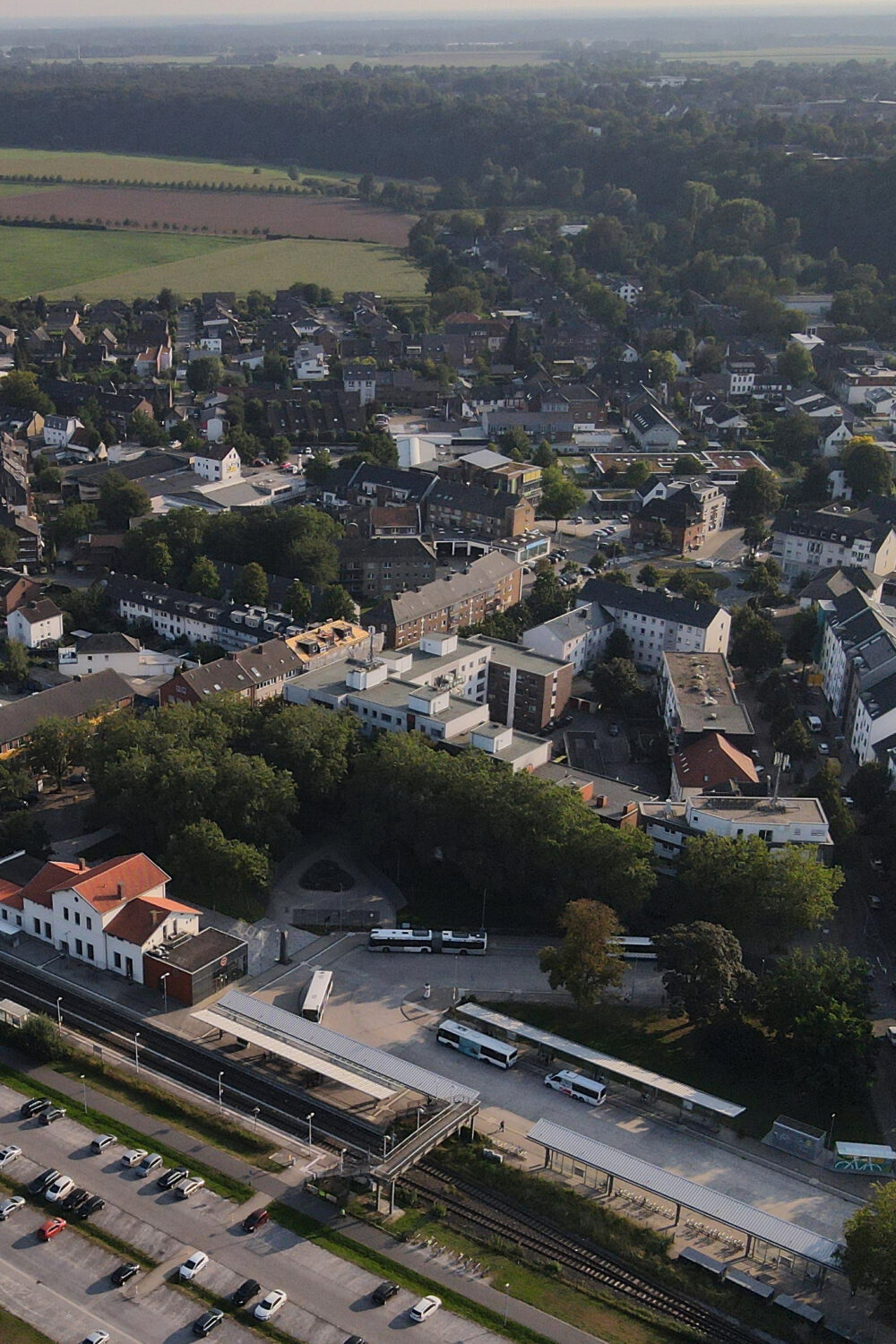 Luftaufnahme von Kleve mit Bahnhof, Parkplätzen, Wohnhäusern und Feldern im Hintergrund bei Tageslicht.