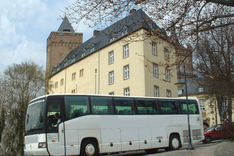 Weißer Reisebus vor der Schwanenburg, im Vordergrund Baumzweige und eine Straßenlaterne