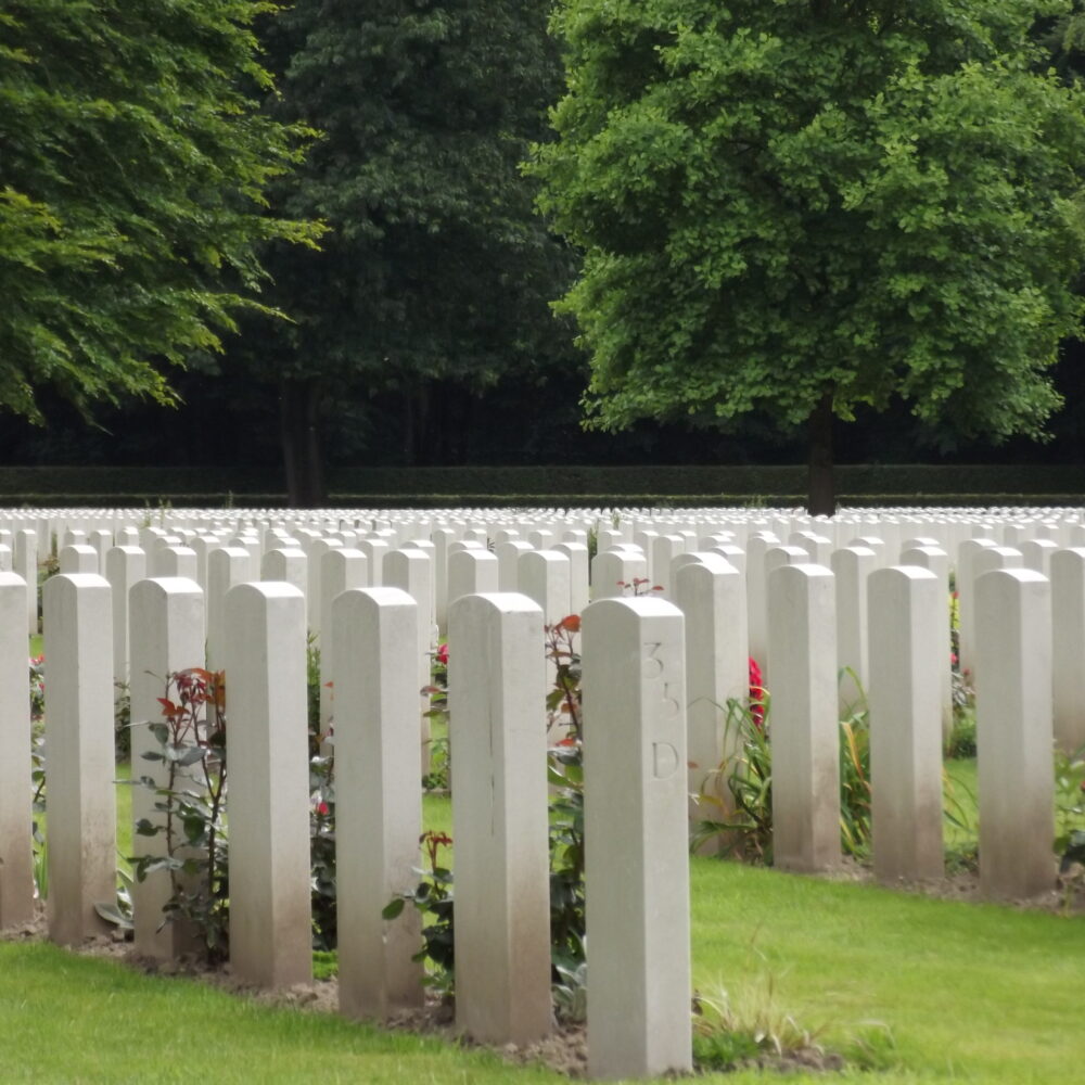 Weiße Grabmale auf dem Britischen Ehrenfriedhof auf einer grünen Wiese, Bäume im Hintergrund