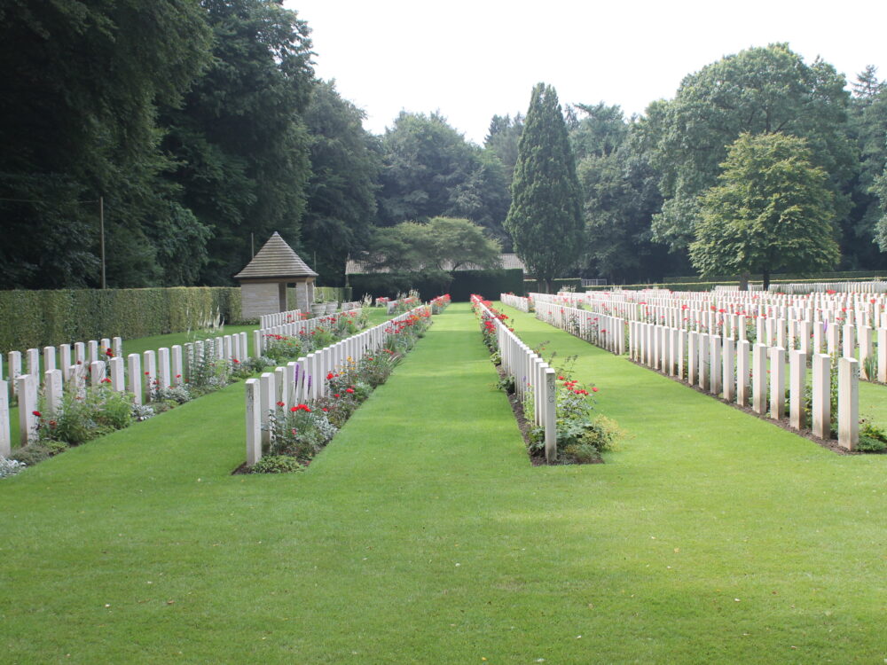Weiße Grabmale auf dem Britischen Ehrenfriedhof auf einer grünen Wiese, Bäume im Hintergrund