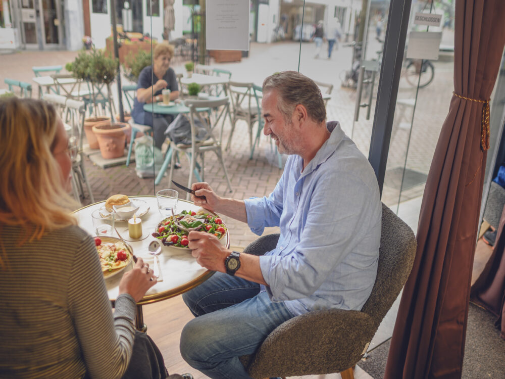 Ein weibliche Person und eine männliche Person sitzen an einem Tisch und essen Salat