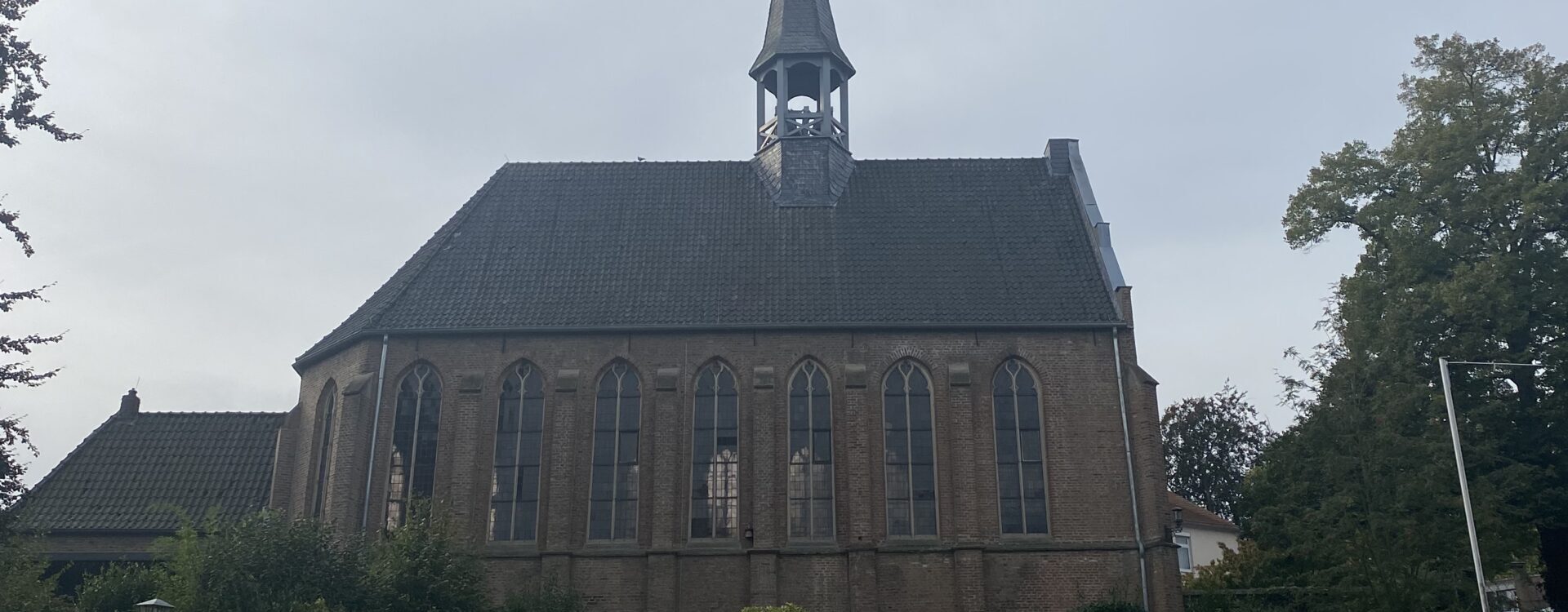Die Kleine Evangelische Kirche mit einem spitzen Turm und großen Fenstern, umgeben von Bäumen und einem gepflegten Garten.
