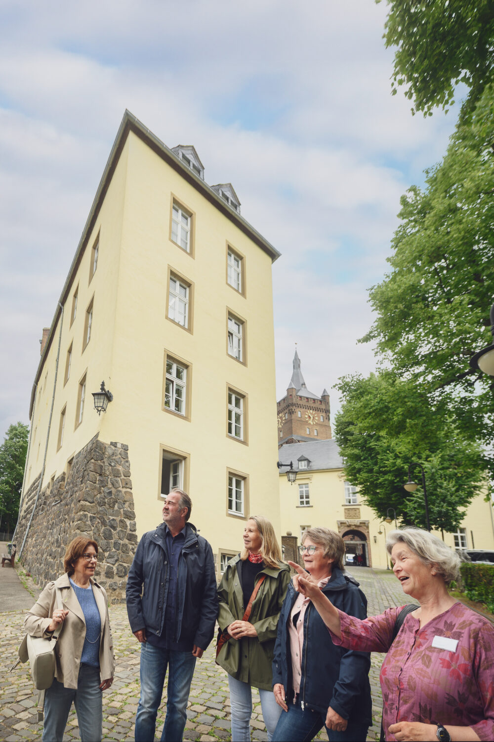 Gruppe von sechs Personen bei einer Führung an der Schwanenburg, eine Person erklärt etwas. Im Hintergrund ist der Turm der Schwanenburg sichtbar.