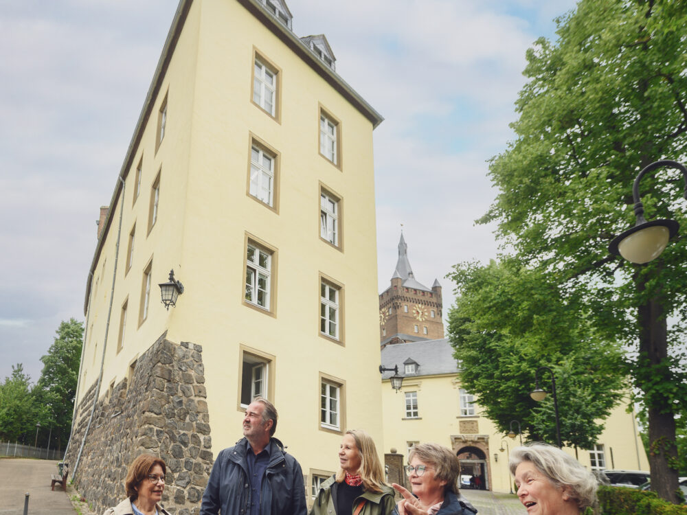 Gruppe von sechs Personen bei einer Führung an der Schwanenburg, eine Person erklärt etwas. Im Hintergrund ist der Turm der Schwanenburg sichtbar.