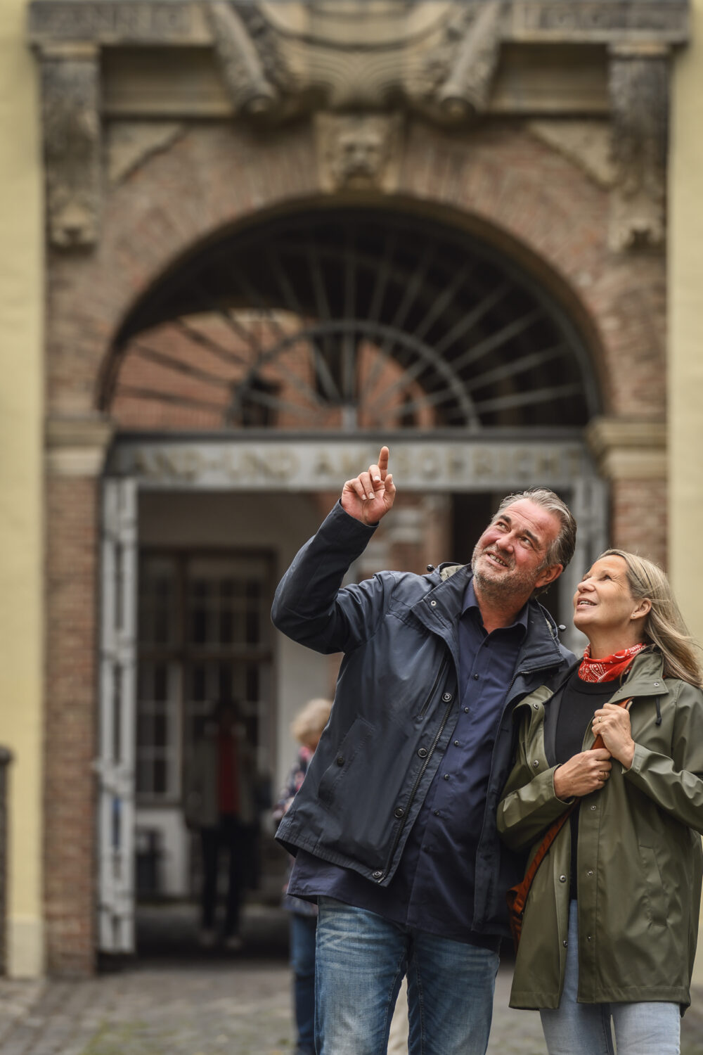Zwei Personen stehen vor einem historischen Torbogen mit Laternen an der Schwanenburg an den Seiten, eine Person zeigt nach oben.