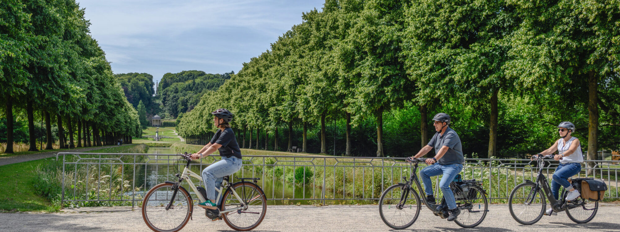 Drei Radfahrer fahren entlang der Gartenanlagen