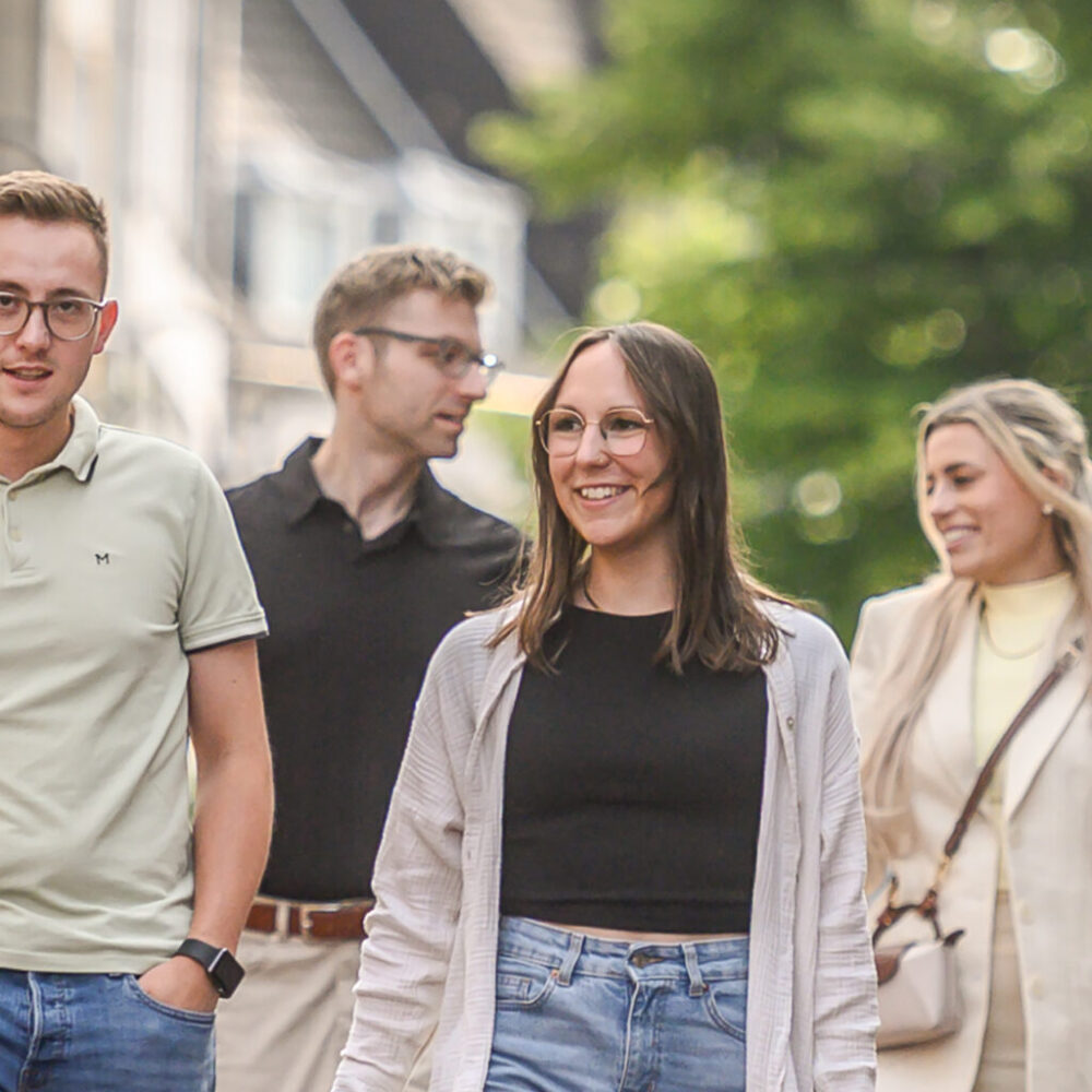 Vier Personen gehen auf einer gepflasterten Fußgängerzone, zwei Männer und zwei Frauen, alle lässig gekleidet, einer trägt eine Einkaufstüte in Kleve.