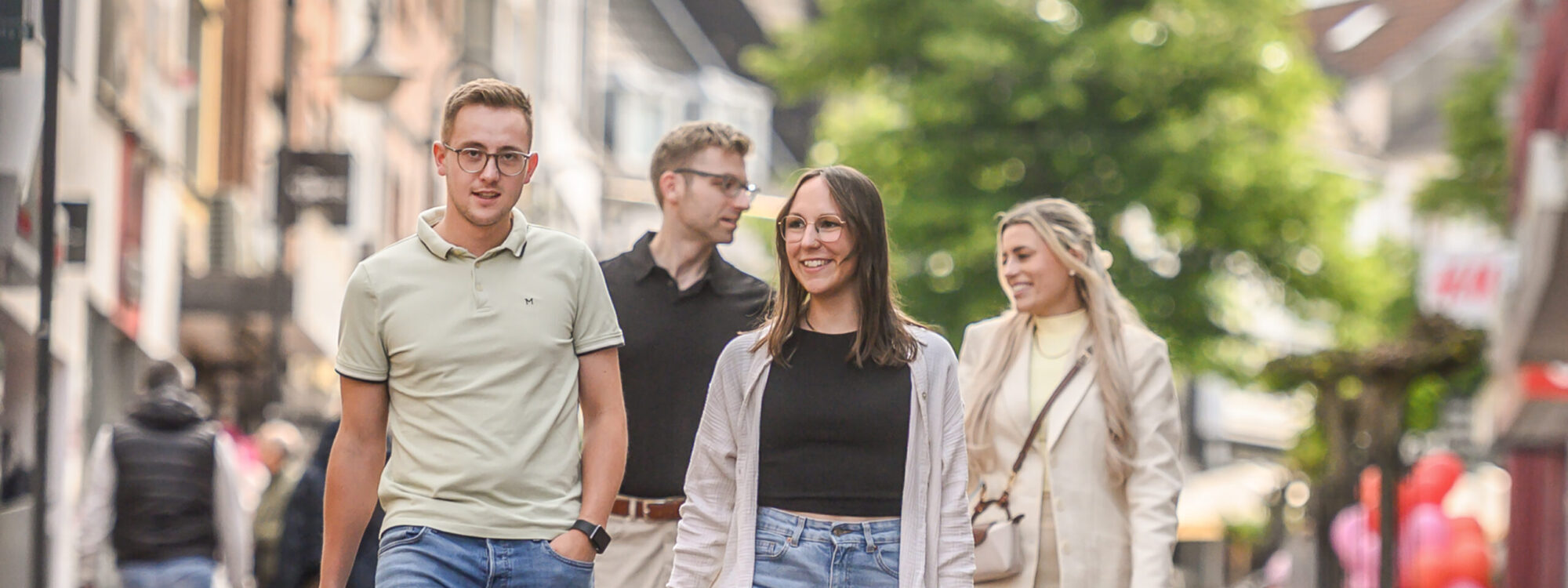 Vier Personen gehen auf einer gepflasterten Fußgängerzone, zwei Männer und zwei Frauen, alle lässig gekleidet, einer trägt eine Einkaufstüte in Kleve.