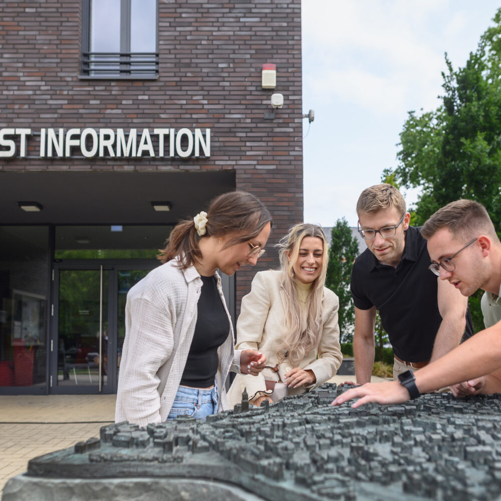 Gruppe vor Tourist-Information betrachtet taktiles Stadtmodell von Kleve auf einem Podest im Freien