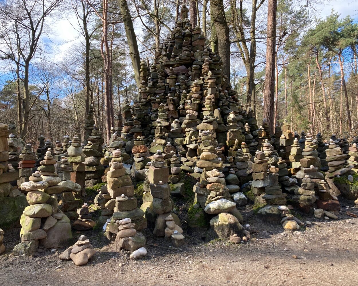 Eine große Ansammlung von Steinmännchen in verschiedenen Größen, angeordnet in einer pyramidenartigen Struktur, umgeben von Bäumen im Wald.
