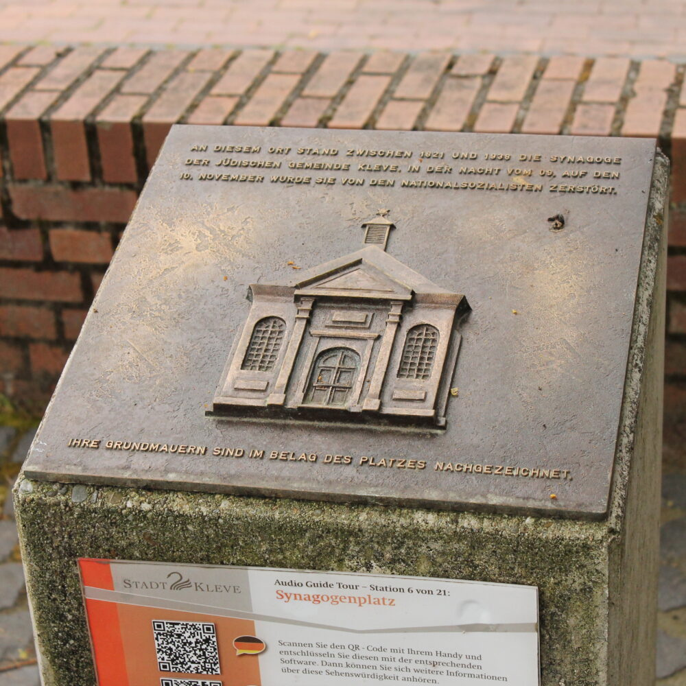 Bronzetafel mit Relief der ehemaligen Synagoge in Kleve, umgeben von Text: 'AN DIESER STAND ZWISCHEN 1827 UND 1938 DIE SYNAGOGE DER JÜDISCHEN GEMEINDE KLEVE...'.
