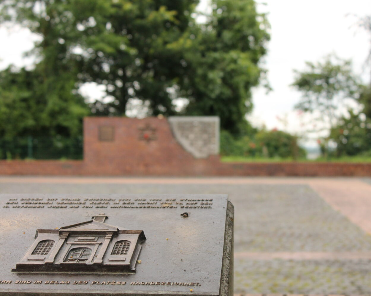 Bronzetafel in Kleve mit Relief einer Synagoge im Vordergrund, im Hintergrund eine Mauer mit einem Davidstern. Text auf der Tafel: 'Hier stand die Synagoge, die 1938 zerstört wurde.'