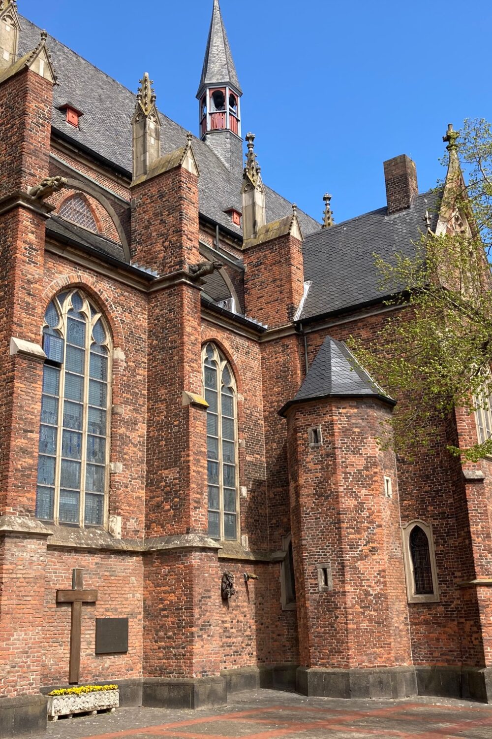 Die Stiftskirche in Kleve, aus rotem Backstein mit mehreren hohen Fenstern und einem spitzen Turm. Im Vordergrund steht eine Statue.