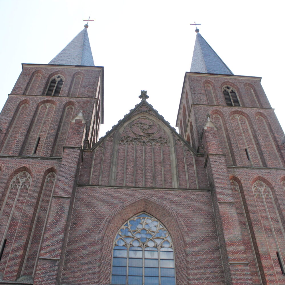 Fassade der Stiftskirche mit zwei hohen, spitzen Türmen, Ziegelsteinmauerwerk und einem großen, gotischen Fenster in der Mitte.