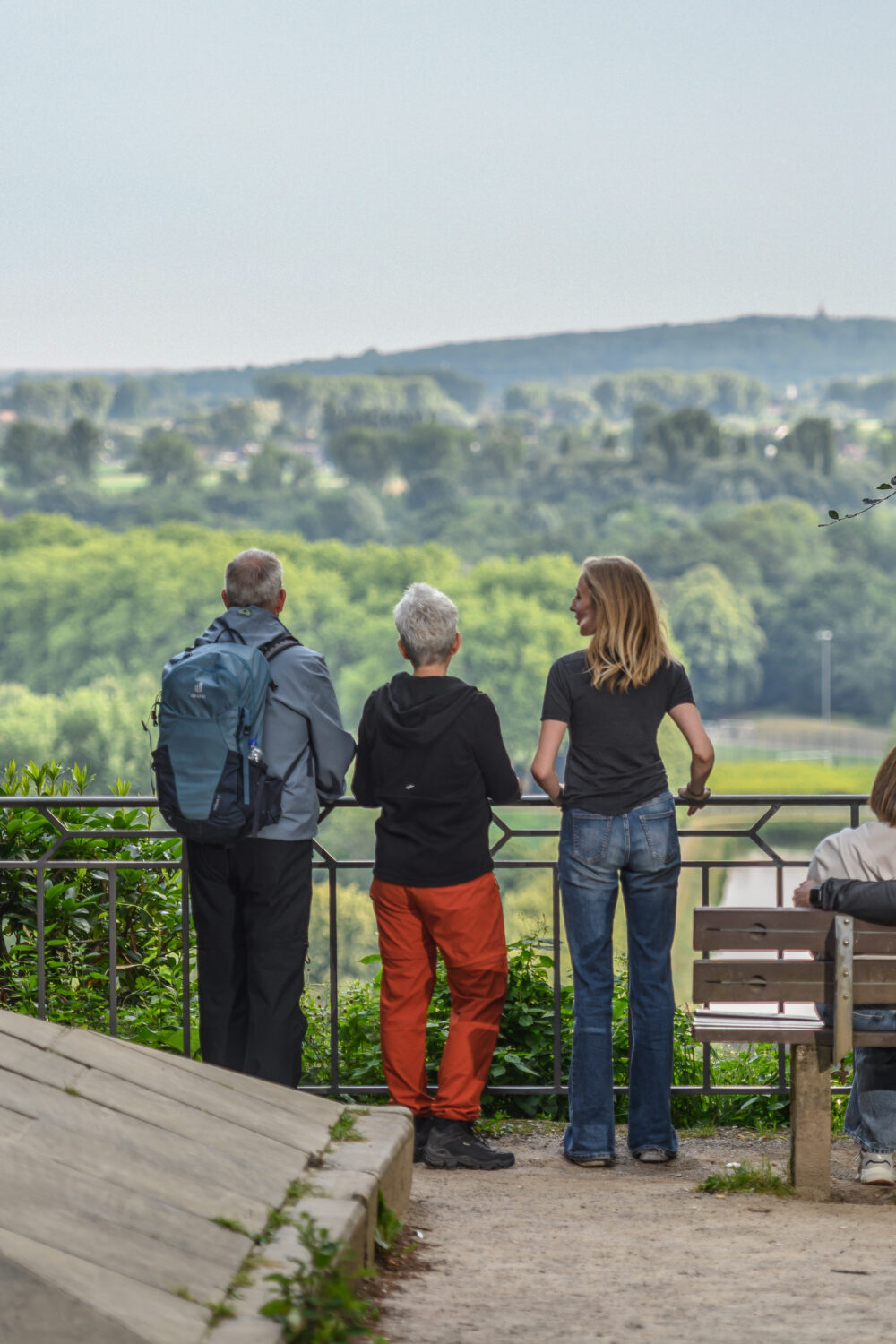 Mehrere Personen stehen und sitzen auf einer Aussichtsplattform am Kupfernen Knopf mit Blick auf bewaldete Hügel und eine Stadt im Hintergrund.