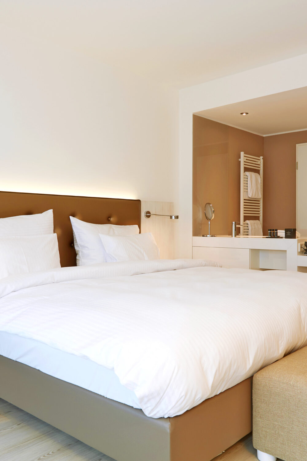 Modern eingerichtetes Hotelzimmer im elaya hotel kleve mit großem Doppelbett, weißer Bettwäsche, Schreibtisch mit rotem Stuhl und Bad mit Glasdusche