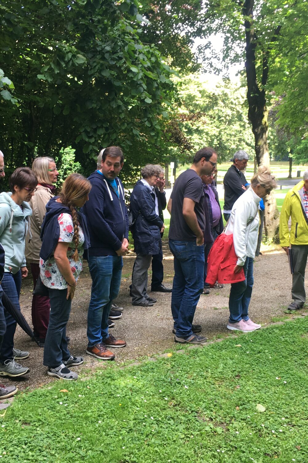 Gruppe von Menschen steht auf einem Weg in den historischen Gartenanlagen von Kleve, ein Mann zeigt auf etwas im Gras neben dem Weg, umgeben von Bäumen.