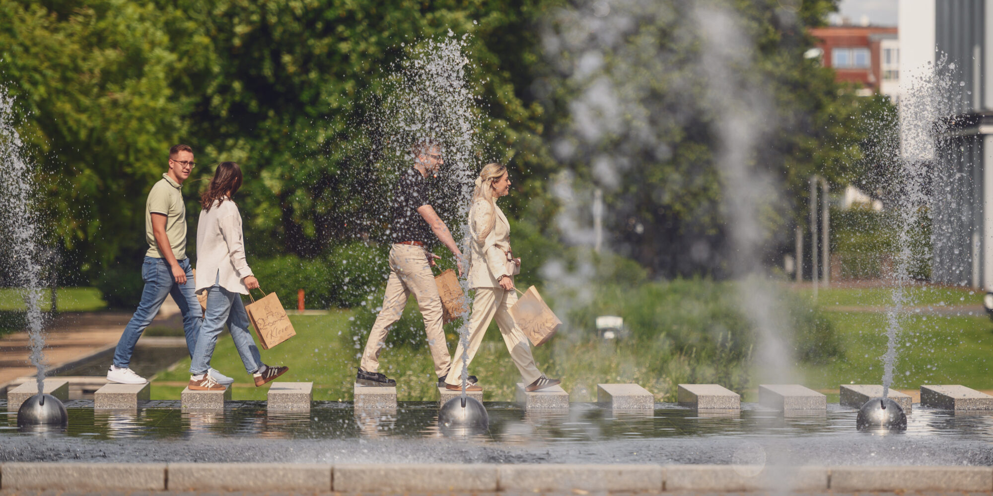 Eine Gruppe von jungen Menschen läuft mit Tüten an einem Wasserspiel vorbei