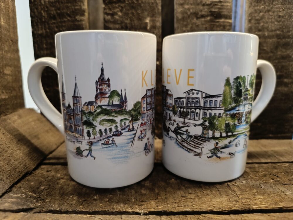 Zwei weiße Tassen mit farbigen Stadtansichten und dem Schriftzug 'KLEVE', die auf einer Holzoberfläche stehen.