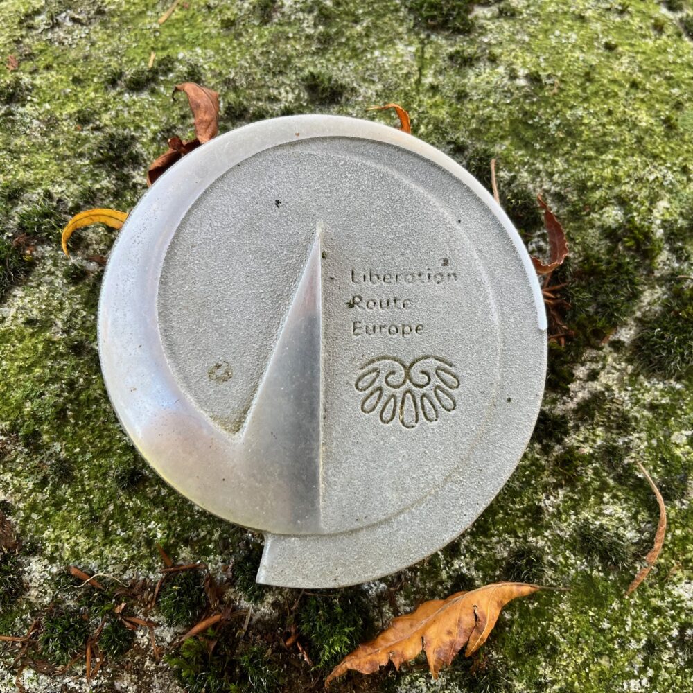 Plakette der Liberation Route in Form eines Vektors auf einem mit Moos bewachsenen Untergrund