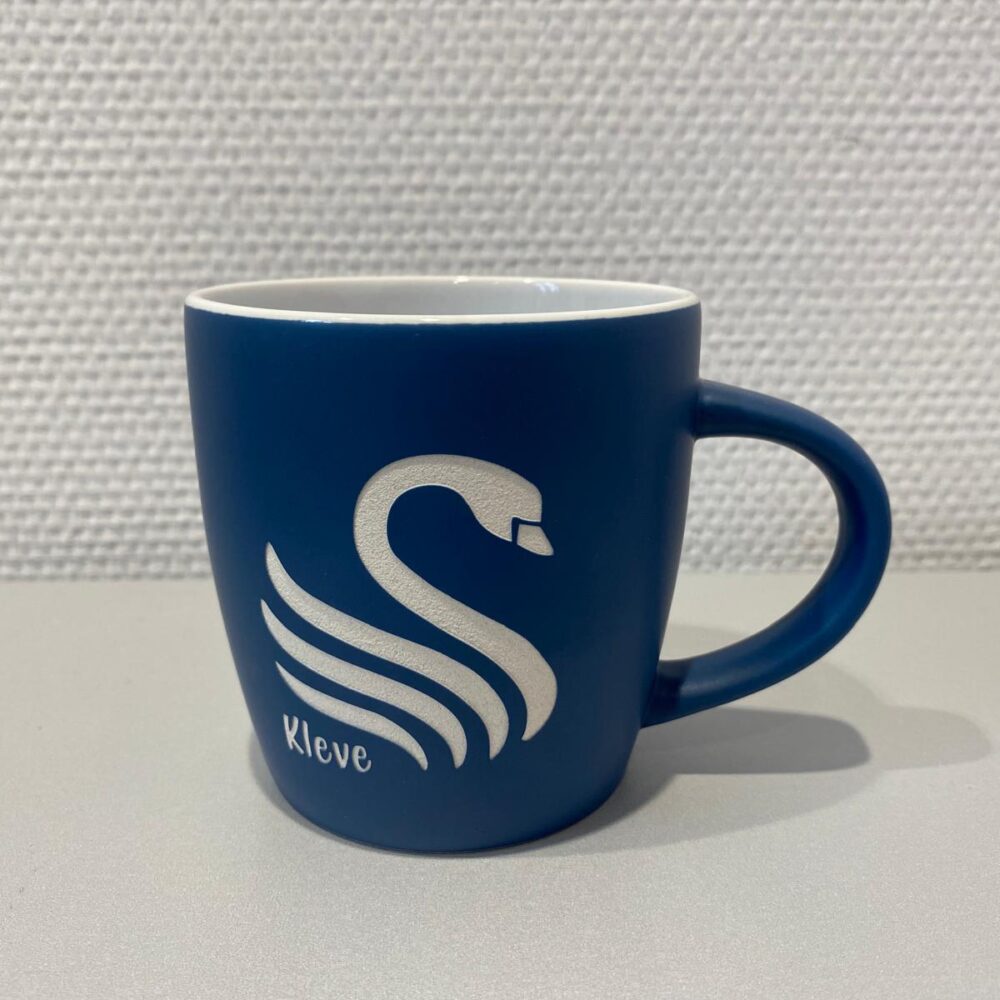 Blaue Keramiktasse mit weißem Schwanenmotiv und weißer Lasergravur 'Kleve'.