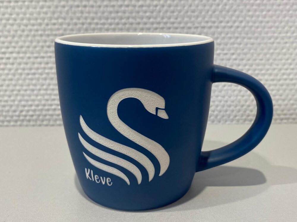 Blaue Keramiktasse mit weißem Schwanenmotiv und weißer Lasergravur 'Kleve'.