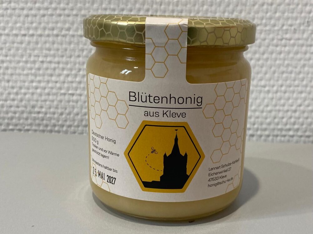 Glas mit Blütenhonig aus Kleve, etikettiert mit einem sechseckigen Wabenmuster und einer schwarzen Silhouette der Schwanenburg mit einer Biene auf gelbem Hintergrund.