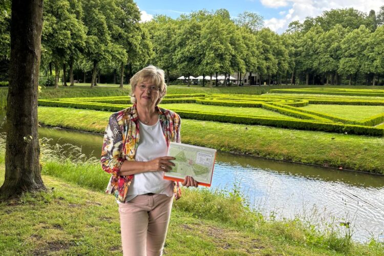 Turguiden står under et tre, med en kanal og en øy i bakgrunnen, og viser et bilde.