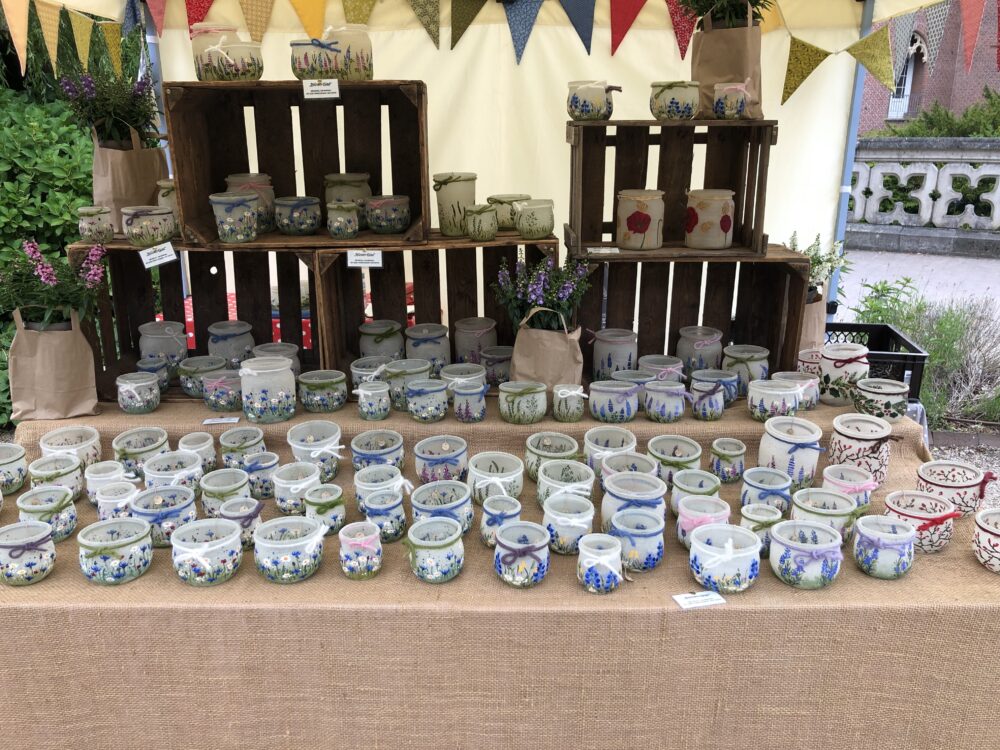 Tisch mit handbemalten Keramikgefäßen mit floralen Motiven vor Holzkisten und bunten Wimpeln