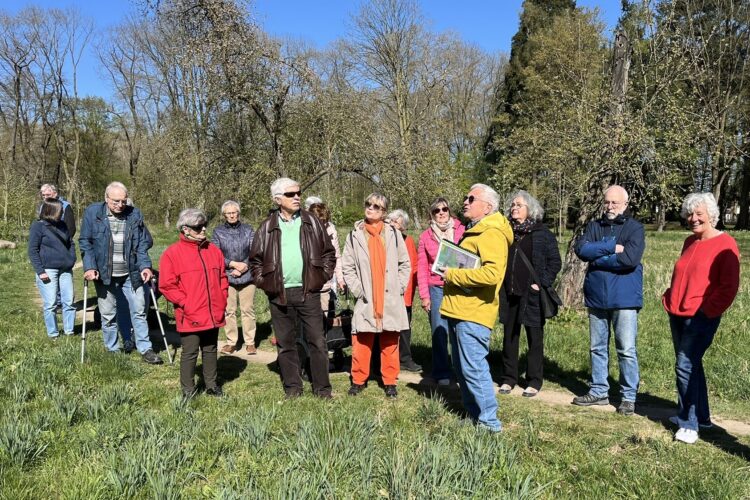 Mehrere Menschen stehen bei einer Führung auf einer frühlingshaften Wiese mit Obstbäumen