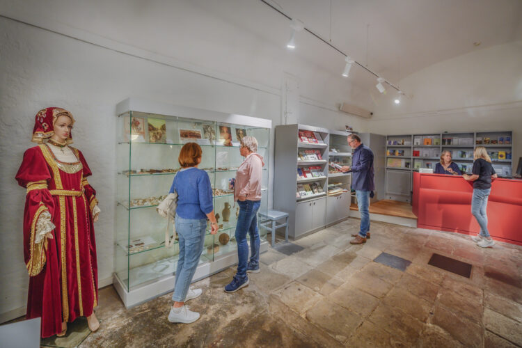 Innenraum des Schwanenturms mit Ausstellungsstücken in Vitrinen, Besuchern und einer Person hinter einem roten Empfangstresen