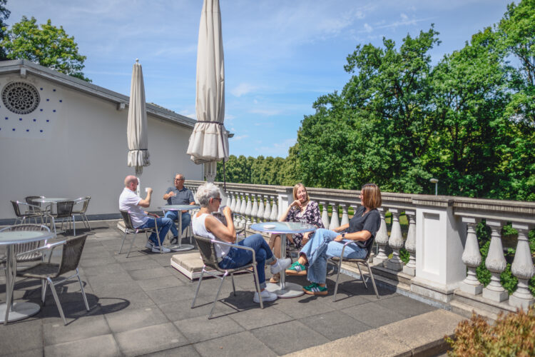 Mehrere Personen sitzen auf der Dachterrasse des Museum Kurhaus Kleve an Tischen mit zugeklappten Sonnenschirmen