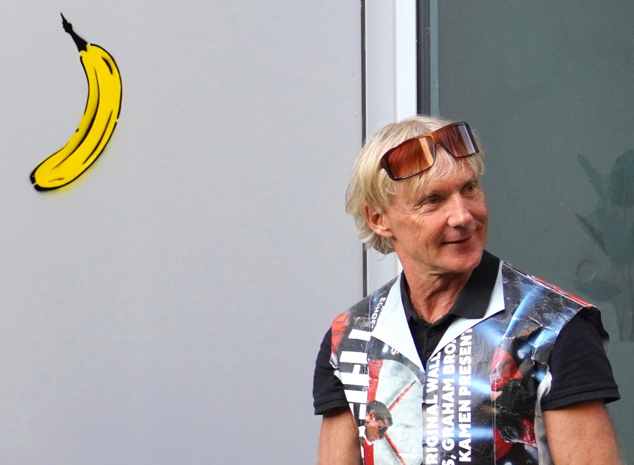 Thomas Baumgärtel mit bunter Weste und hochgeschobener Brille, links oben im Bild eine Banane