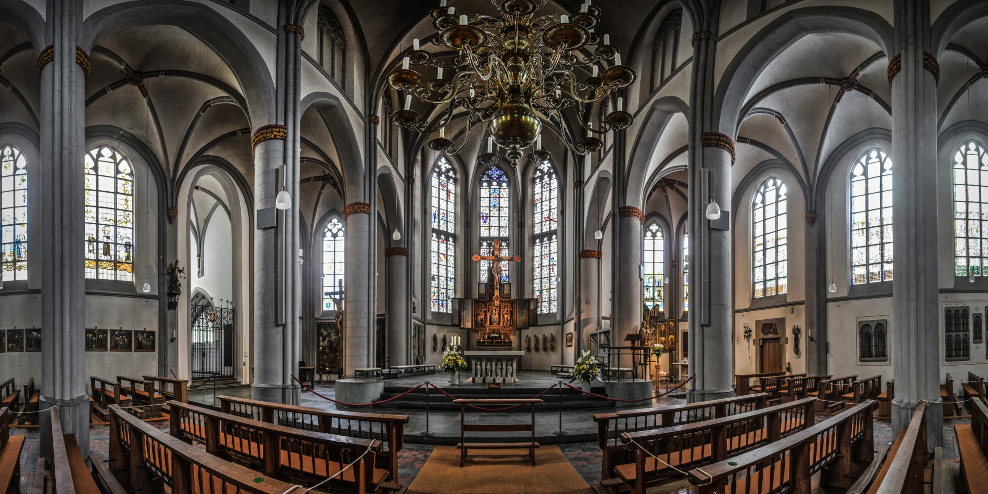 Innenraum einer Kirche mit hohen Säulen, Spitzbogenfenstern und einem Altar mit Kreuz und Kerzen
