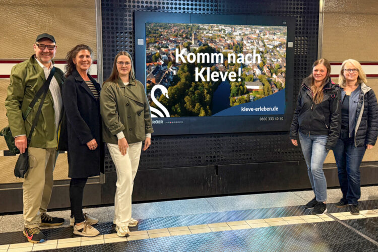 Fünf Personen stehen vor einem Werbescreen in der einer U-Bahn-Station