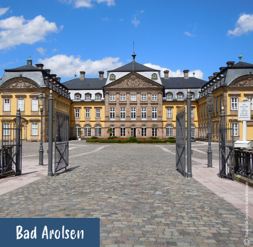 Offenes schmiedeeisernes Tor mit Blick auf ein barockes Schlossgebäude mit gelben Fassaden unter blauem Himmel