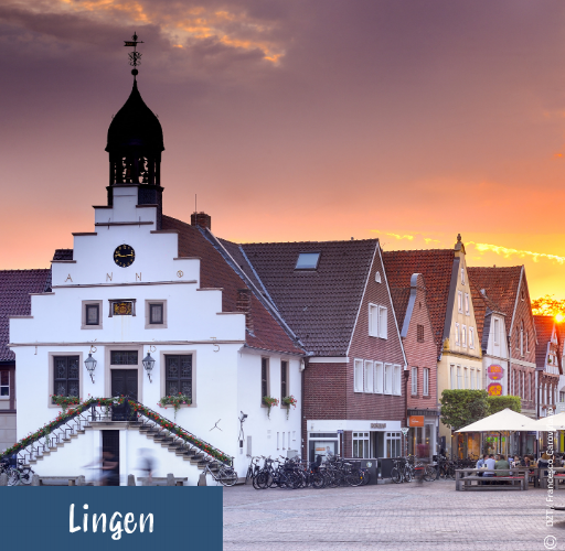 Historisches Rathaus mit Treppenaufgängen und Glockenturm vor einem Sonnenuntergang in einer Altstadt mit Fachwerkhäusern und Kopfsteinpflaster in Lingen