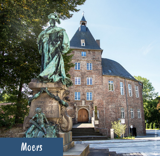 Bronzestatue vor einem historischen Backsteingebäude mit spitzem Dach und mehreren Fenstern in Moers