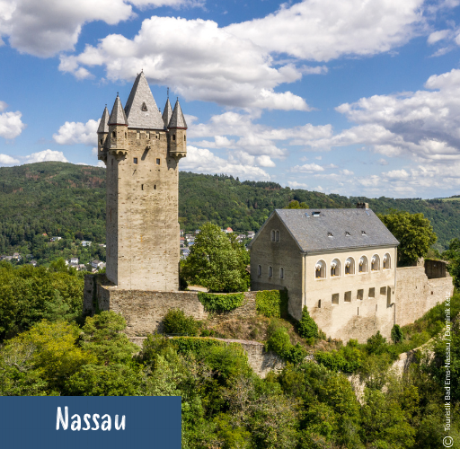 Burg Nassau mit hohem Turm und angrenzendem Gebäude auf bewaldetem Hügel unter blauem Himmel mit Wolken