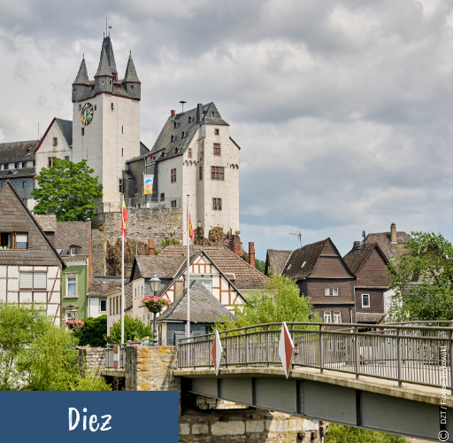 Blick auf die historische Altstadt von Diez mit Fachwerkhäusern, einer Brücke und einem Turm mit Uhr unter bewölktem Himmel