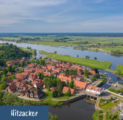 Luftaufnahme von Hitzacker mit roten Dächern, Fluss und grüner Landschaft im Hintergrund