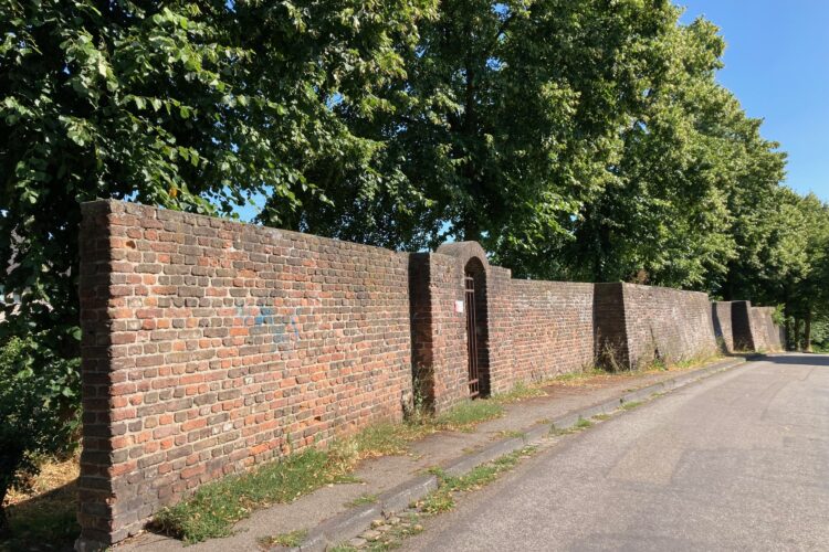 Mauer entlang einer Straße, im Hintergrund sind Bäume zu sehen