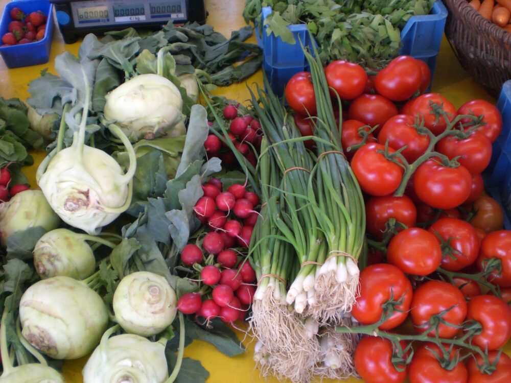 Verschiedene frische Gemüsesorten wie Kohlrabi, Radieschen, Frühlingszwiebeln und Tomaten auf einem Marktstand